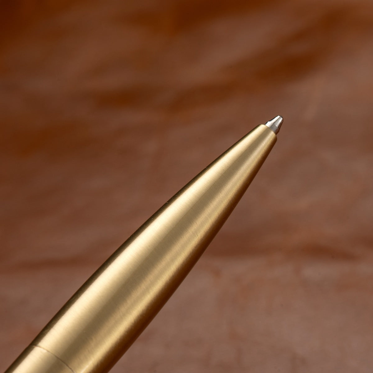 Vintage brass metal pen resting on leather desk surface, classic writing instrument scene
