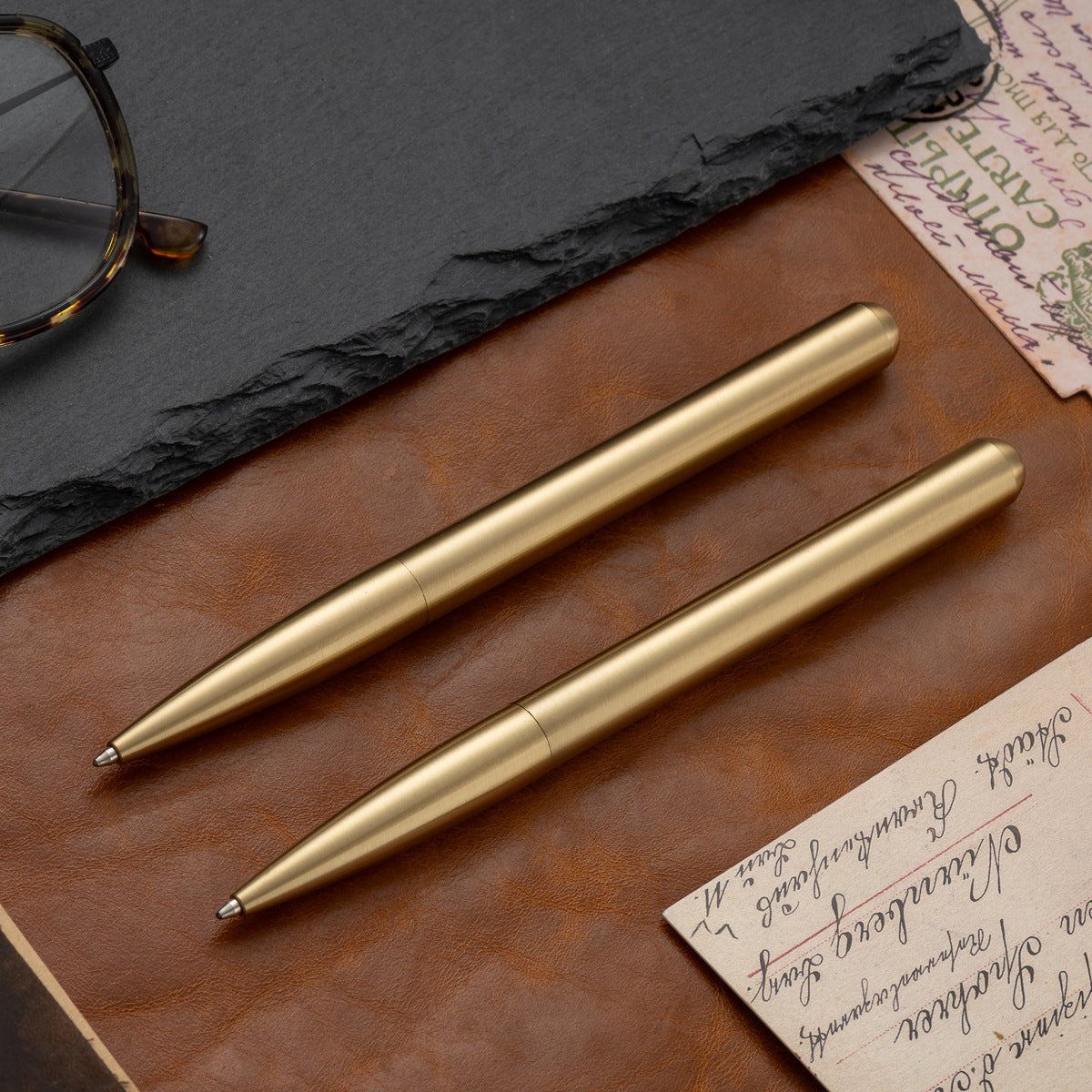 Vintage brass metal pen resting on leather desk surface, classic writing instrument scene
