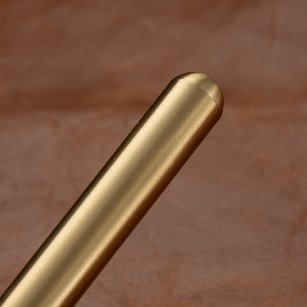 Vintage brass metal pen resting on leather desk surface, classic writing instrument scene
