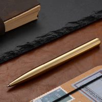 Vintage brass metal pen resting on leather desk surface, classic writing instrument scene
