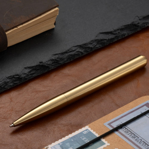 Vintage brass metal pen resting on leather desk surface, classic writing instrument scene
